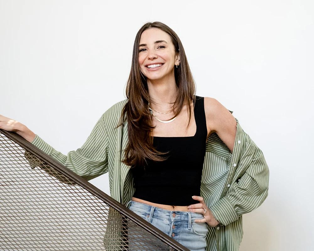 Blaine standing on a staircase, wearing a green shirt over a black tank-top, smiling.