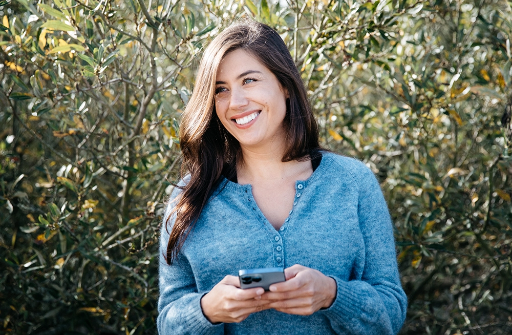 Tara in a blue sweater, holding her phone, smiling