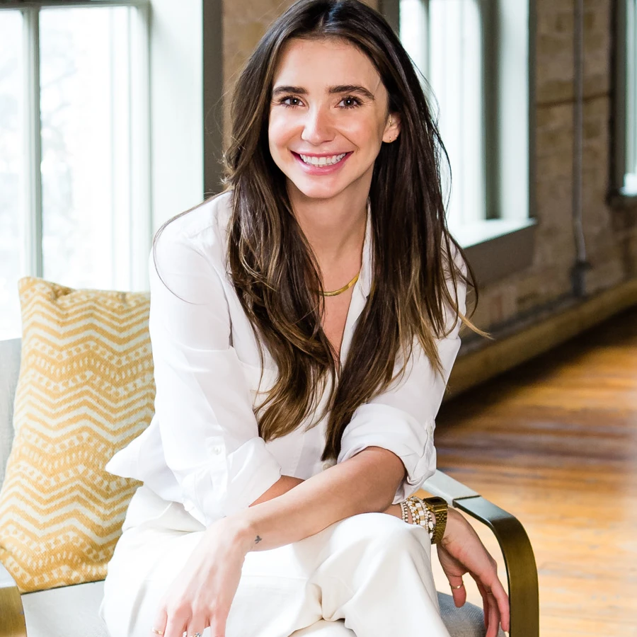 Photo of Blaine in a white outfit in a loft-like building, seated, smiling.