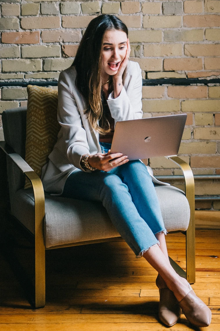 Blaine wearing a white jacket in a loft, looking at her computer, smiling