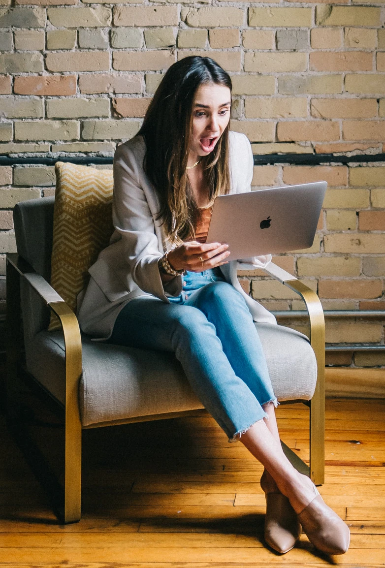 Blaine wearing a white jacket in a loft, looking at her computer, another surprised expression on her face