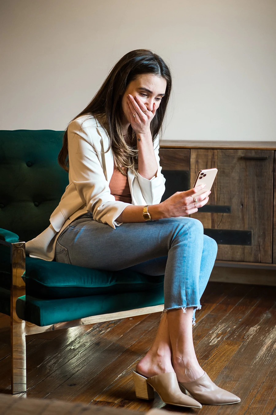 Blaine wearing a white jacket in a loft, looking at her phone, with her hand covering her mouth