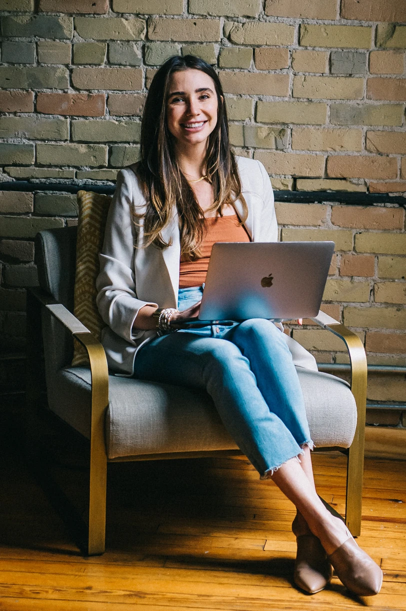 Blaine wearing a white jacket in a loft, looking at her computer, smiling upward